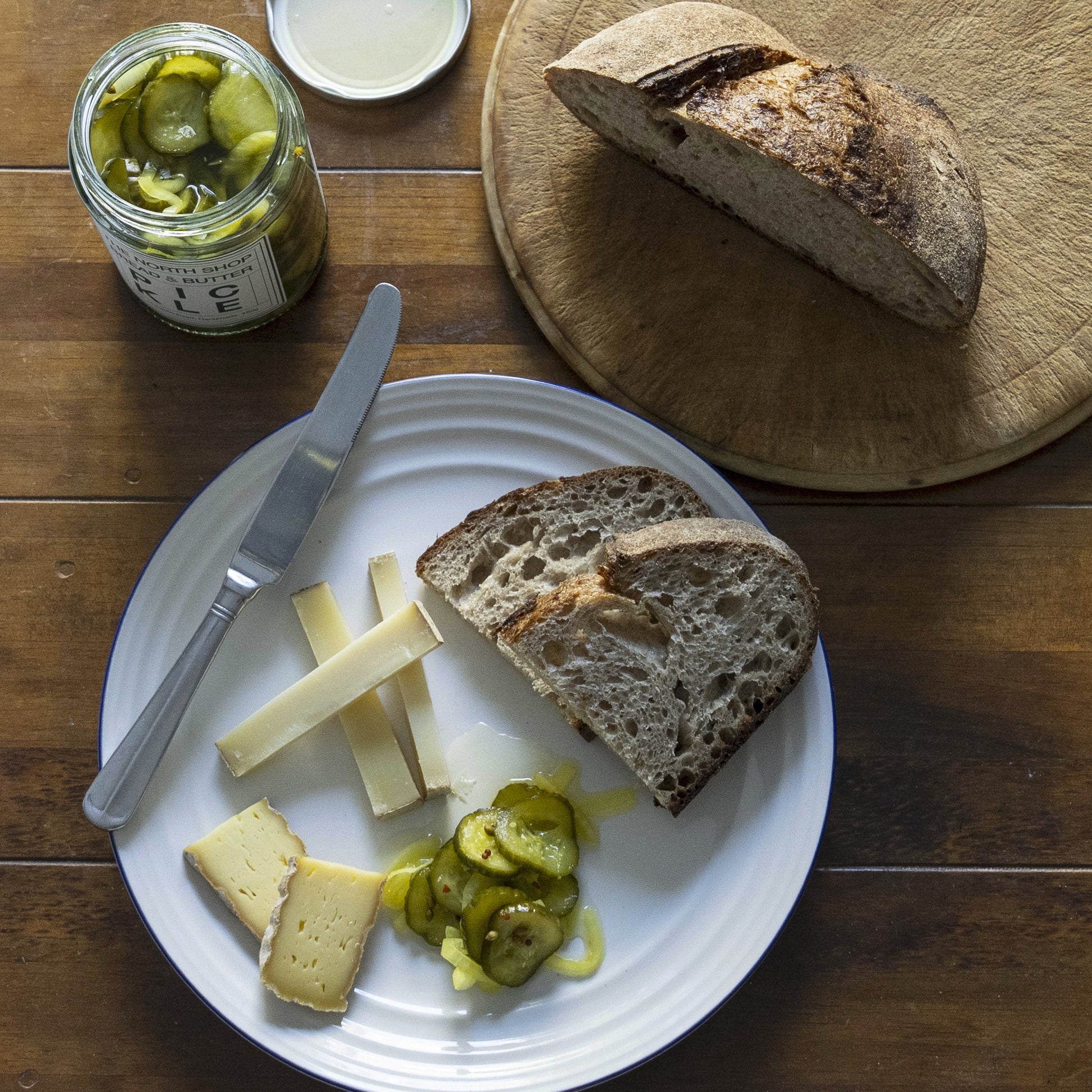 Plated bread, cheese, and pickles on a wooden table