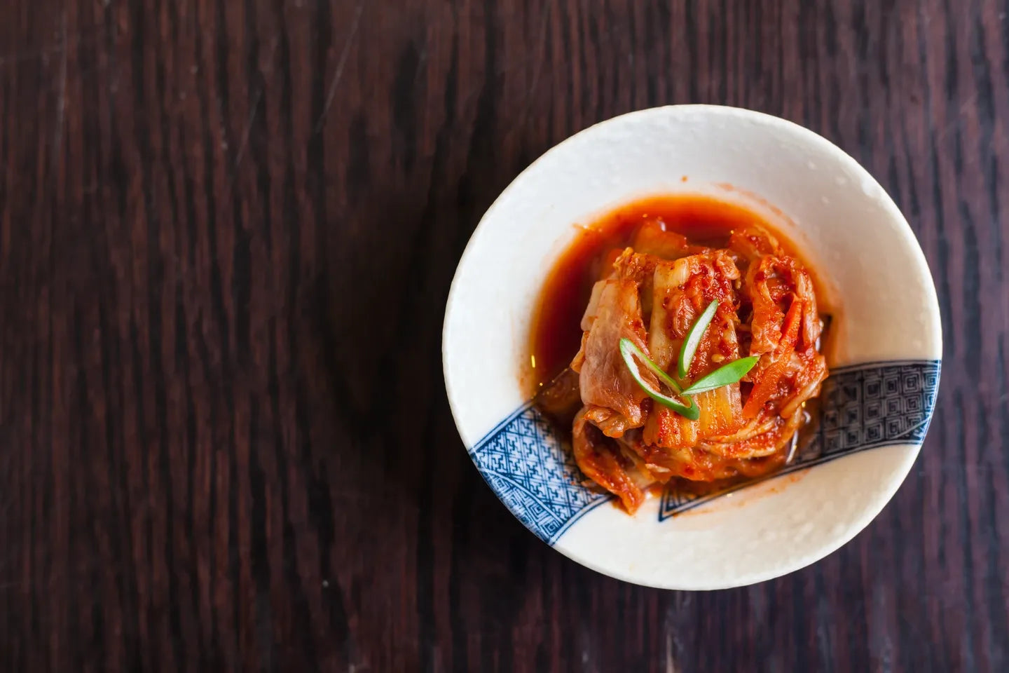 Kimchi in a white ceramic bowl on a dark wooden table.
