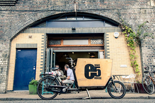Bicycle with a cardboard box labeled 'E5 Bakehouse' parked outside a building with a blue door.