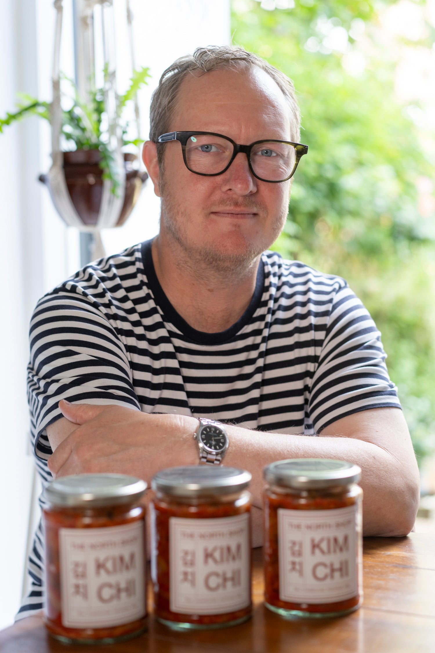 A man sat at a table with three jars of kimchi in front of him.