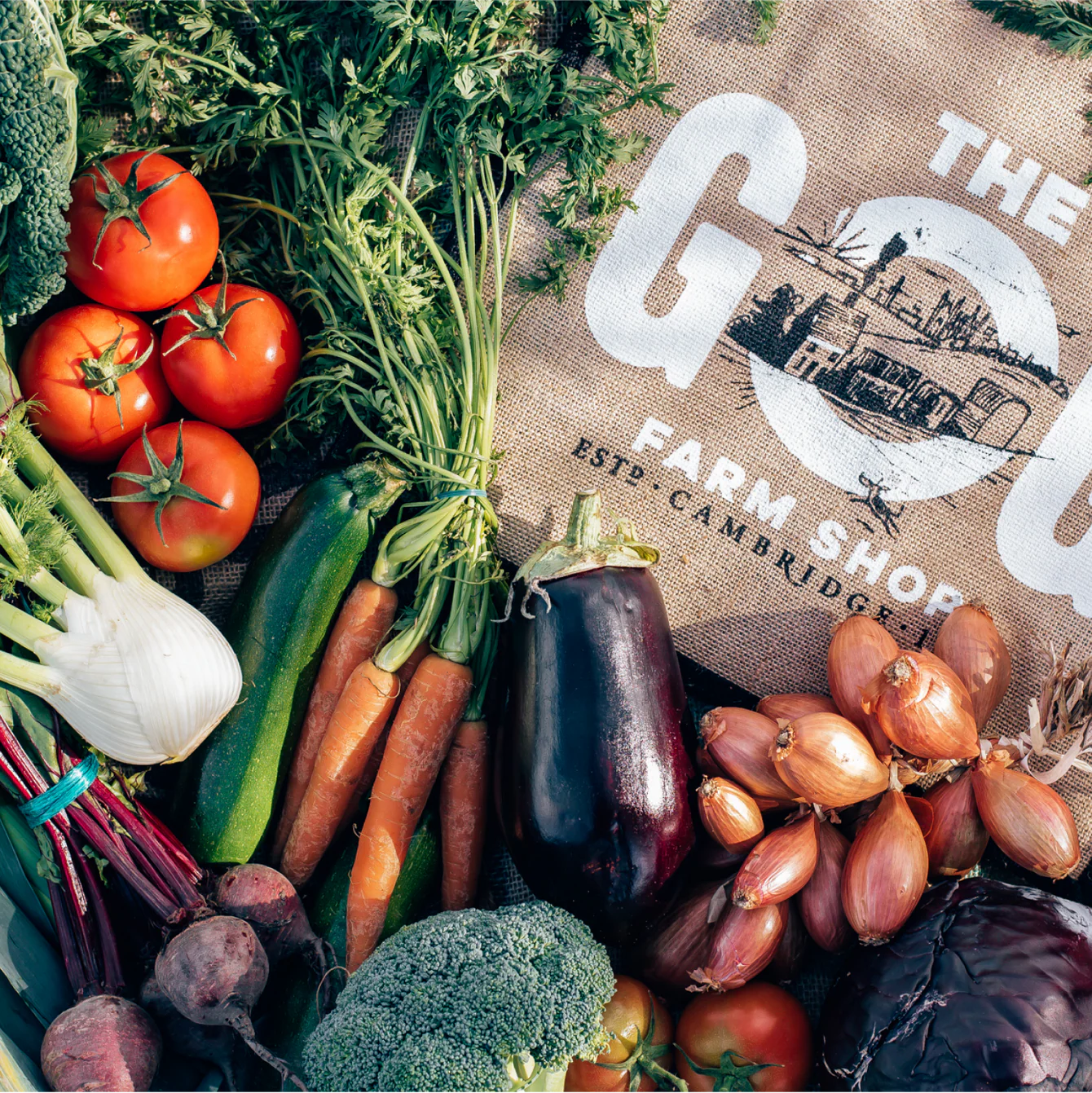 Assorted fresh vegetables on a burlap bag with 'The Gog Farm Shop' branding.