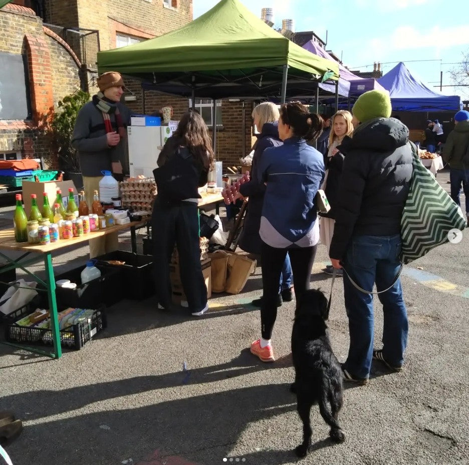 People at an outdoor market with tents and a dog on a leash.